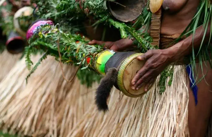 Woman beating a hand-made drum as part of a tribal ceremony. Papua New Guinea.