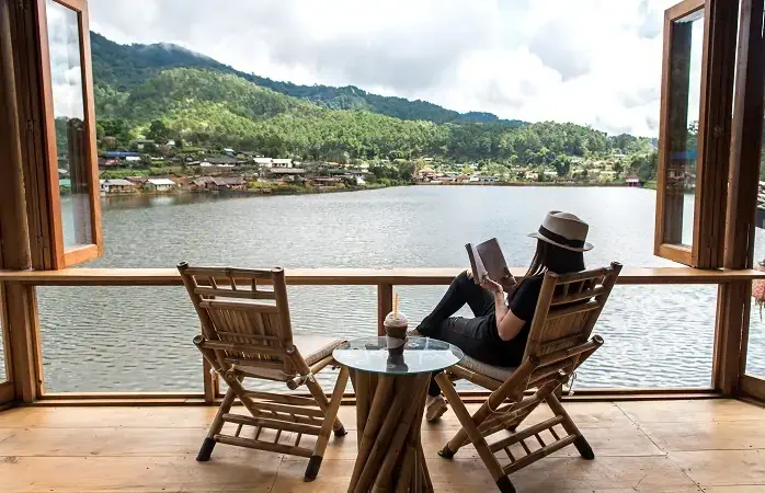 Woman reading a book lying and drink ice coffee on the chair in wood terrace against beautiful view relax and happy day. Lifestyle Concept