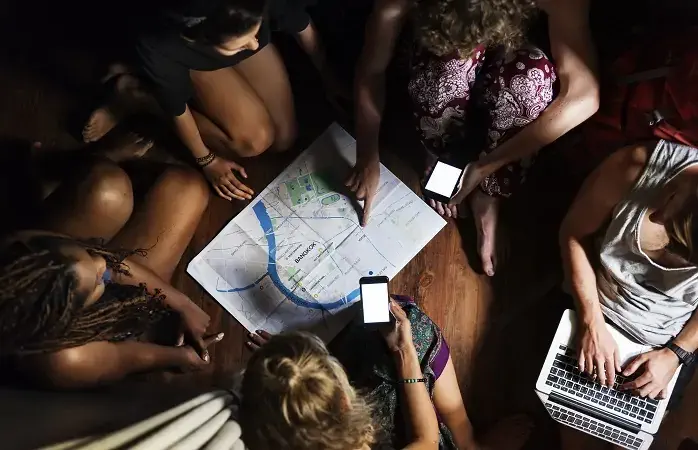 Group of diverse tourists sitting on the wooden floor planning checking on the map