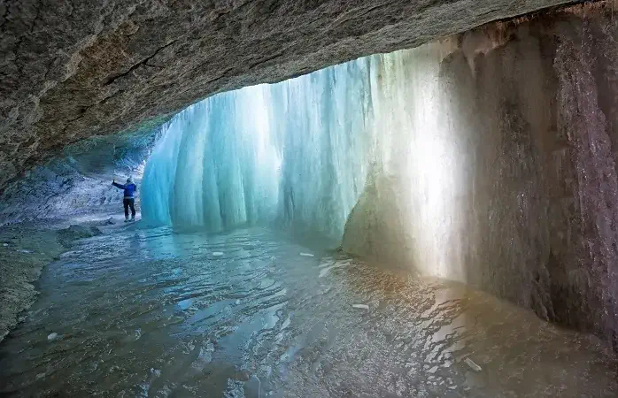 Woman takes a selfie in a grotto behind colorful turquoise tinted ice in a frozen waterfall in winter, Minnehaha Falls, Minneapolis, MN, USA